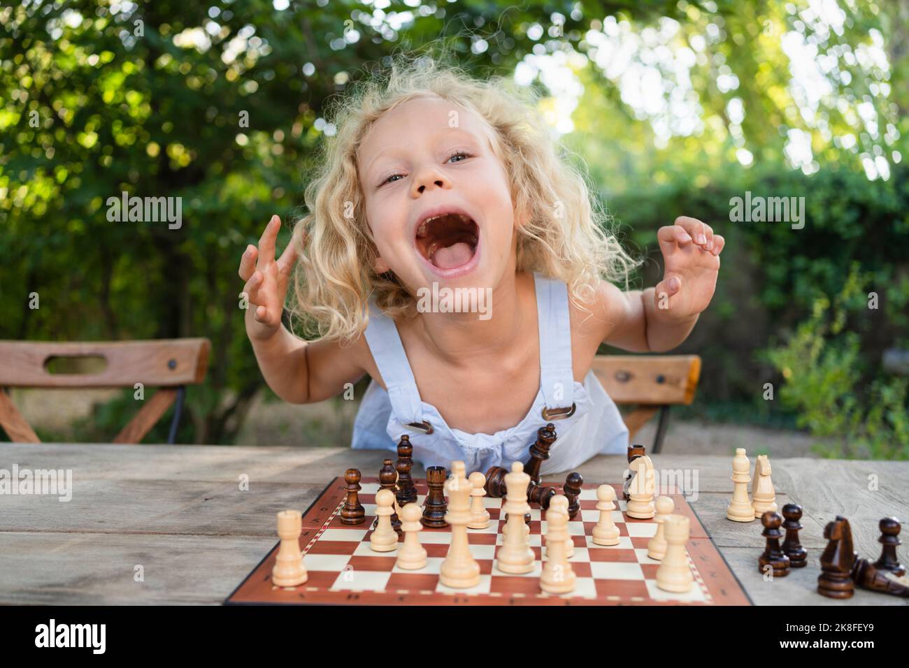 Ragazza eccitata con scacchiera sul tavolo in giardino Foto Stock