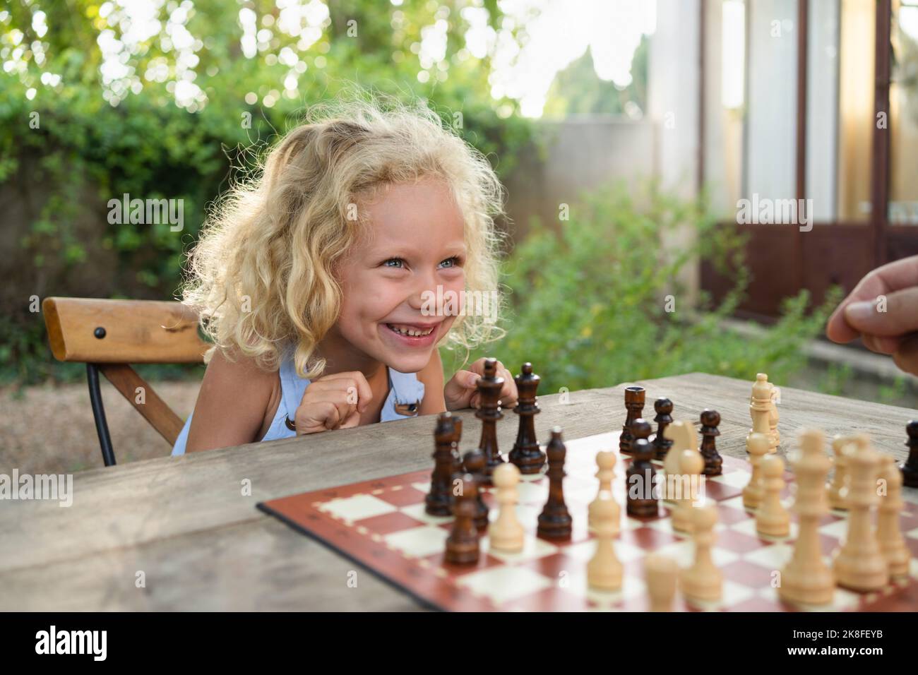 Allegra ragazza bionda con scacchiera sul tavolo in giardino Foto Stock
