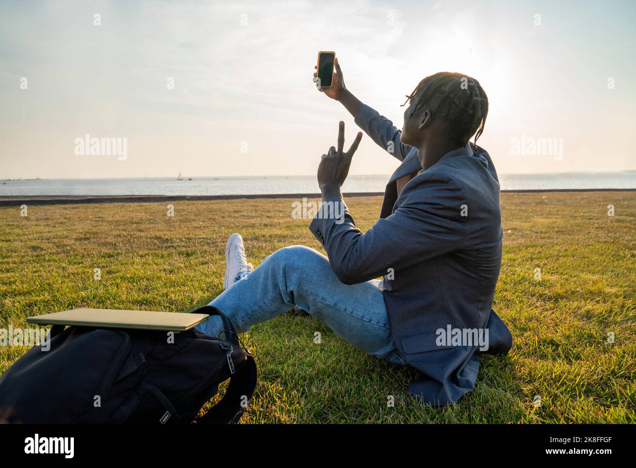 Giovane uomo d'affari che prende selfie attraverso lo smartphone seduto sull'erba Foto Stock