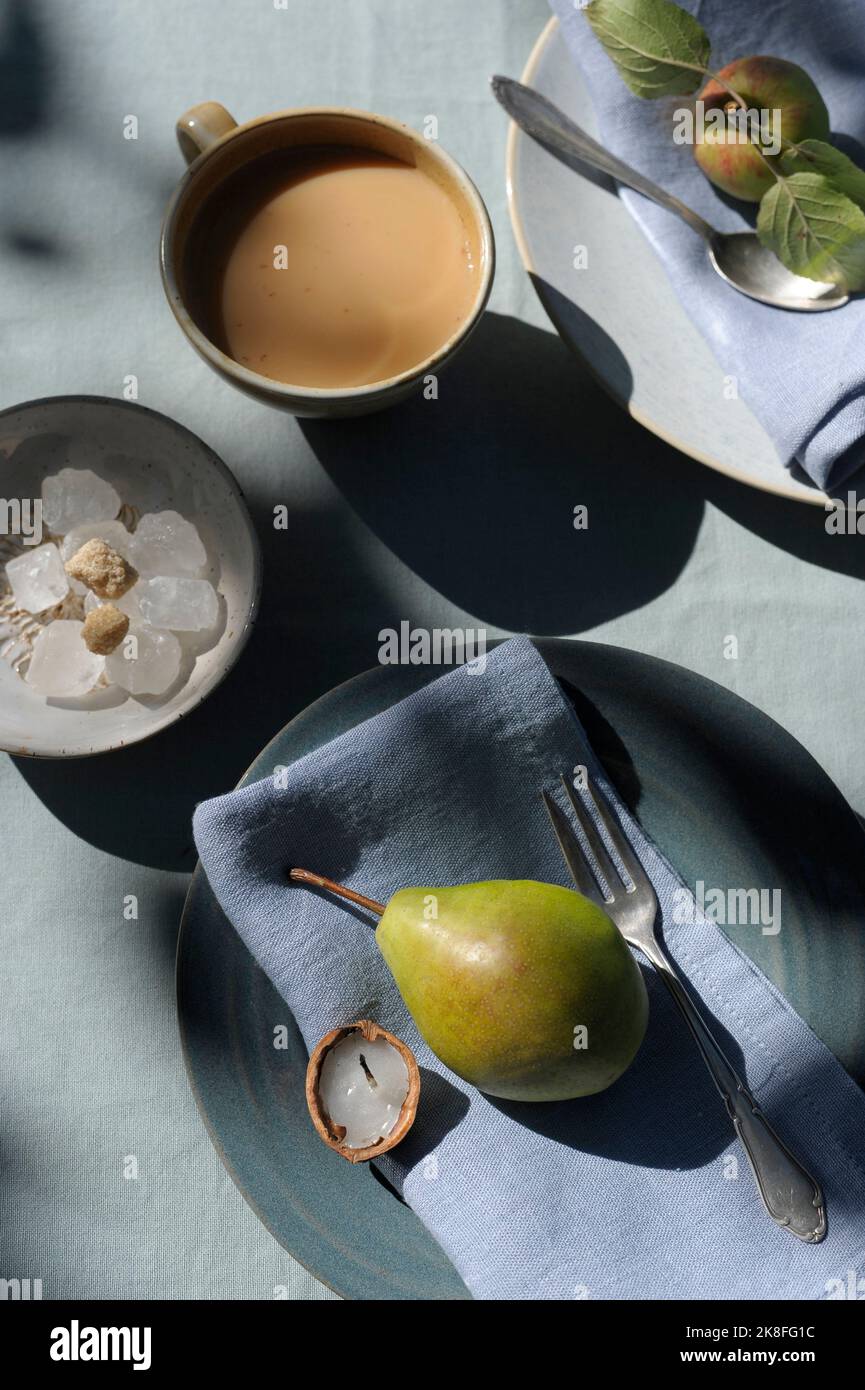 Tazza di caffè, ciotola con cubetti di zucchero, pera, mela, piatti e piccola candela di noce Foto Stock