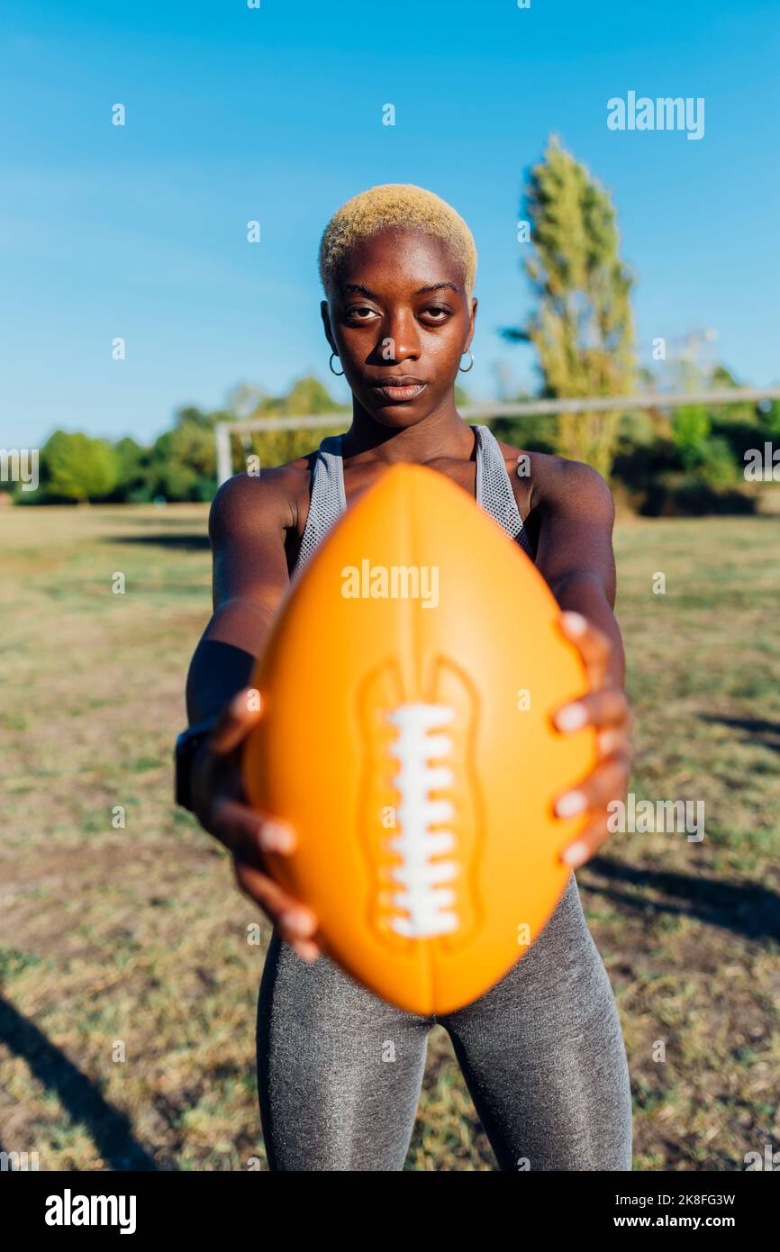 Giocatore sportivo sicuro che tiene il football americano sul campo Foto Stock