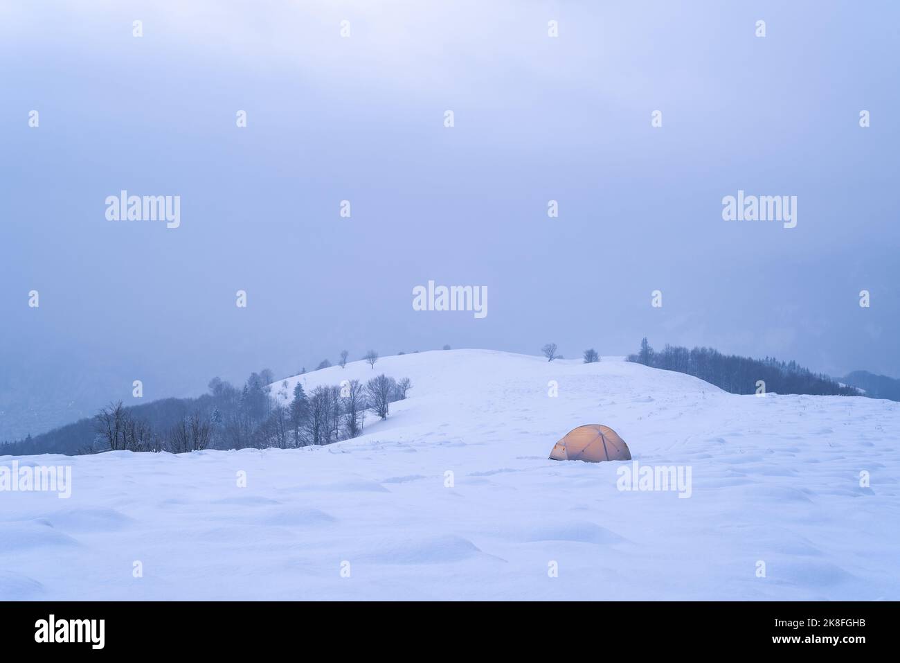 Campeggio invernale con tenda in montagne innevate Foto Stock