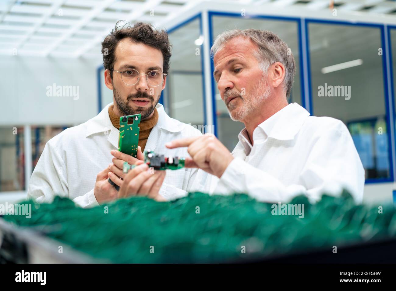 Ingegnere senior che discute su una scheda di circuito con un collega del settore Foto Stock