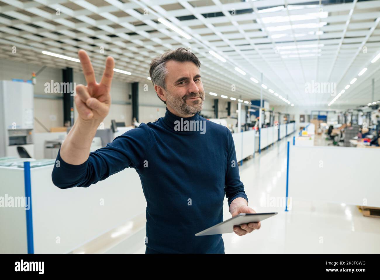Uomo d'affari sorridente con un tablet PC che mostra un gesto di pace nel settore Foto Stock