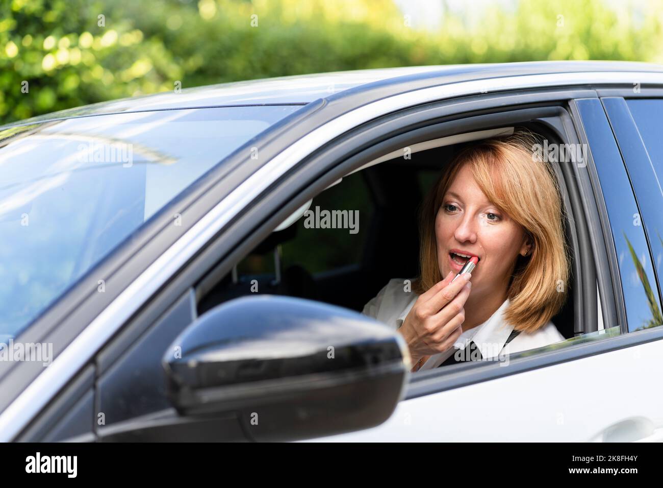 Donna matura che guarda lo specchio di vista laterale dell'auto e applicare il rossetto Foto Stock