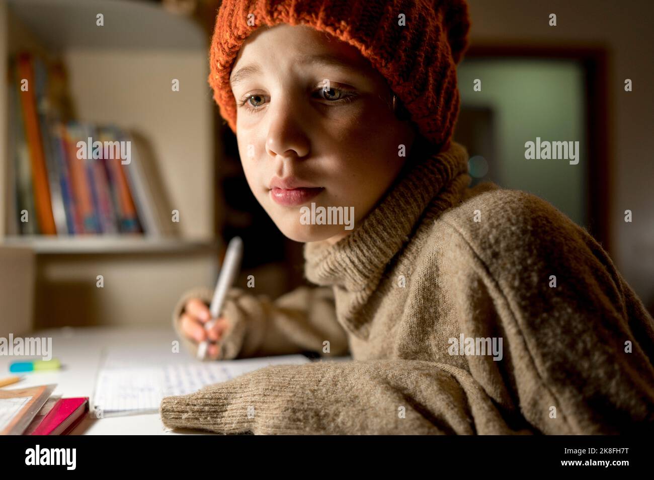 Ragazzo che indossa un maglione e un cappello a maglia che studia a casa Foto Stock