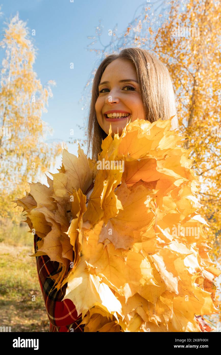 Donna felice con foglie d'acero nel parco nelle giornate di sole Foto Stock