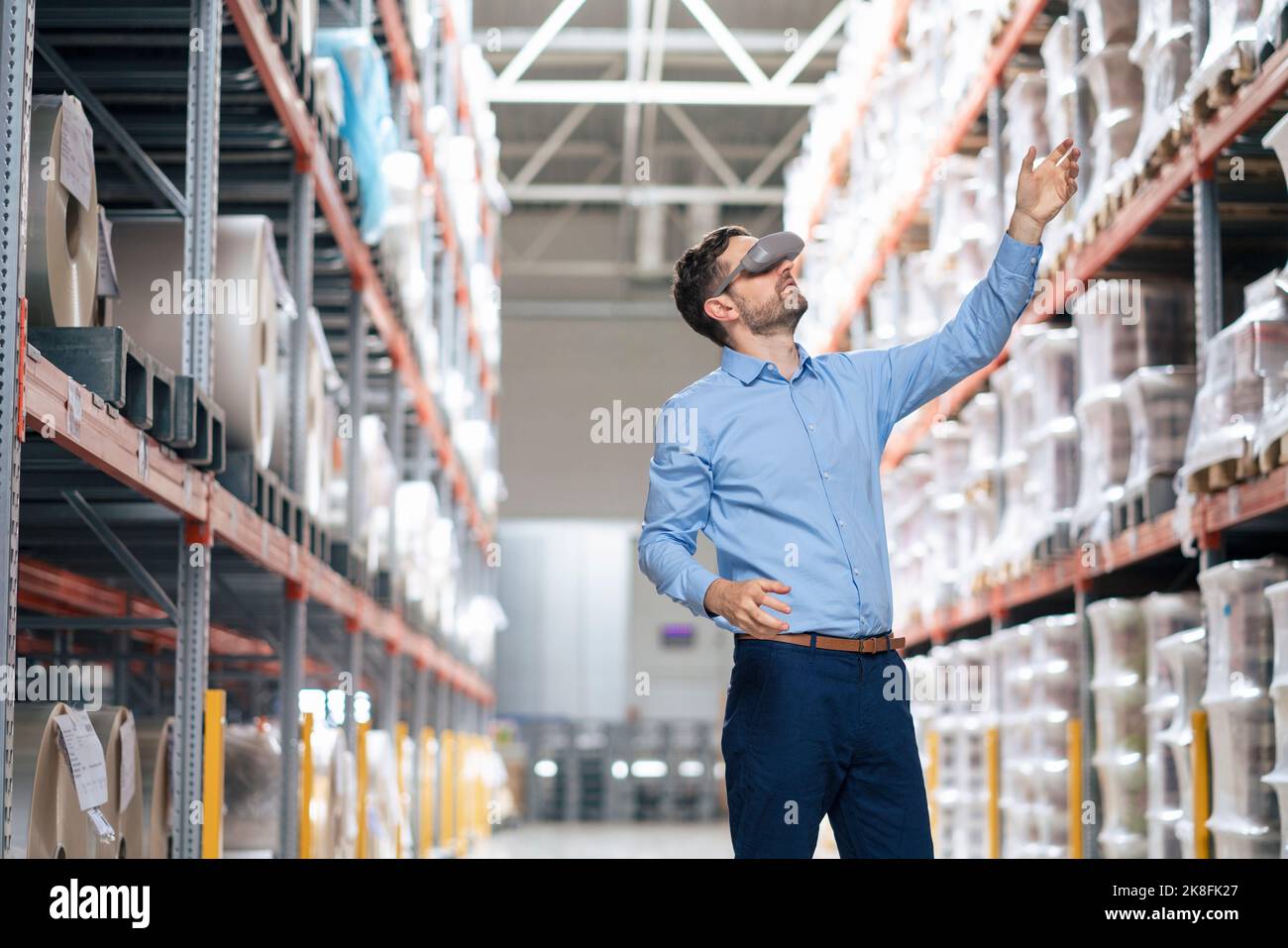 Uomo d'affari che indossa un simulatore di realtà virtuale gesturing in magazzino Foto Stock
