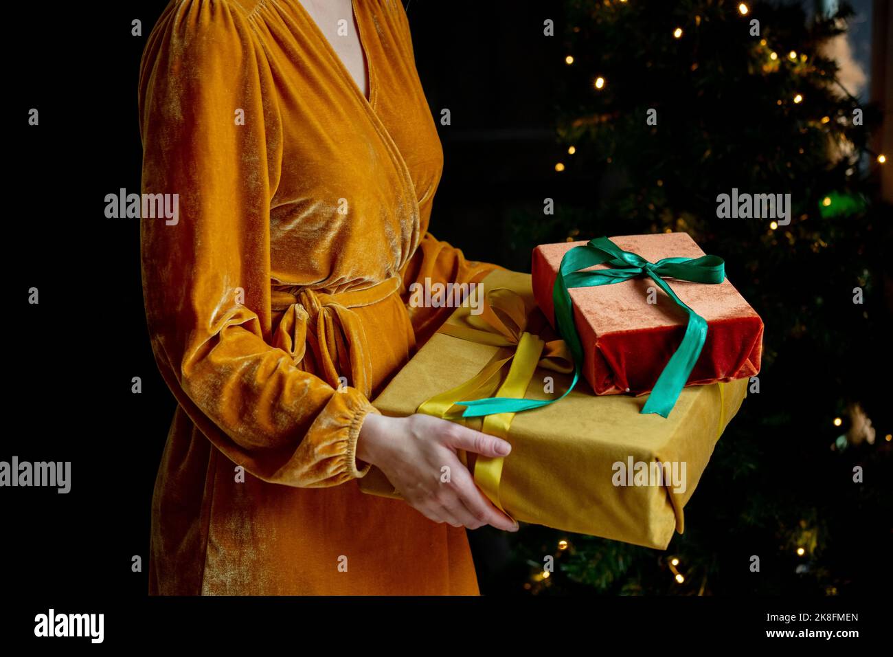 Donna con vestito giallo che tiene regali di Natale a casa Foto Stock