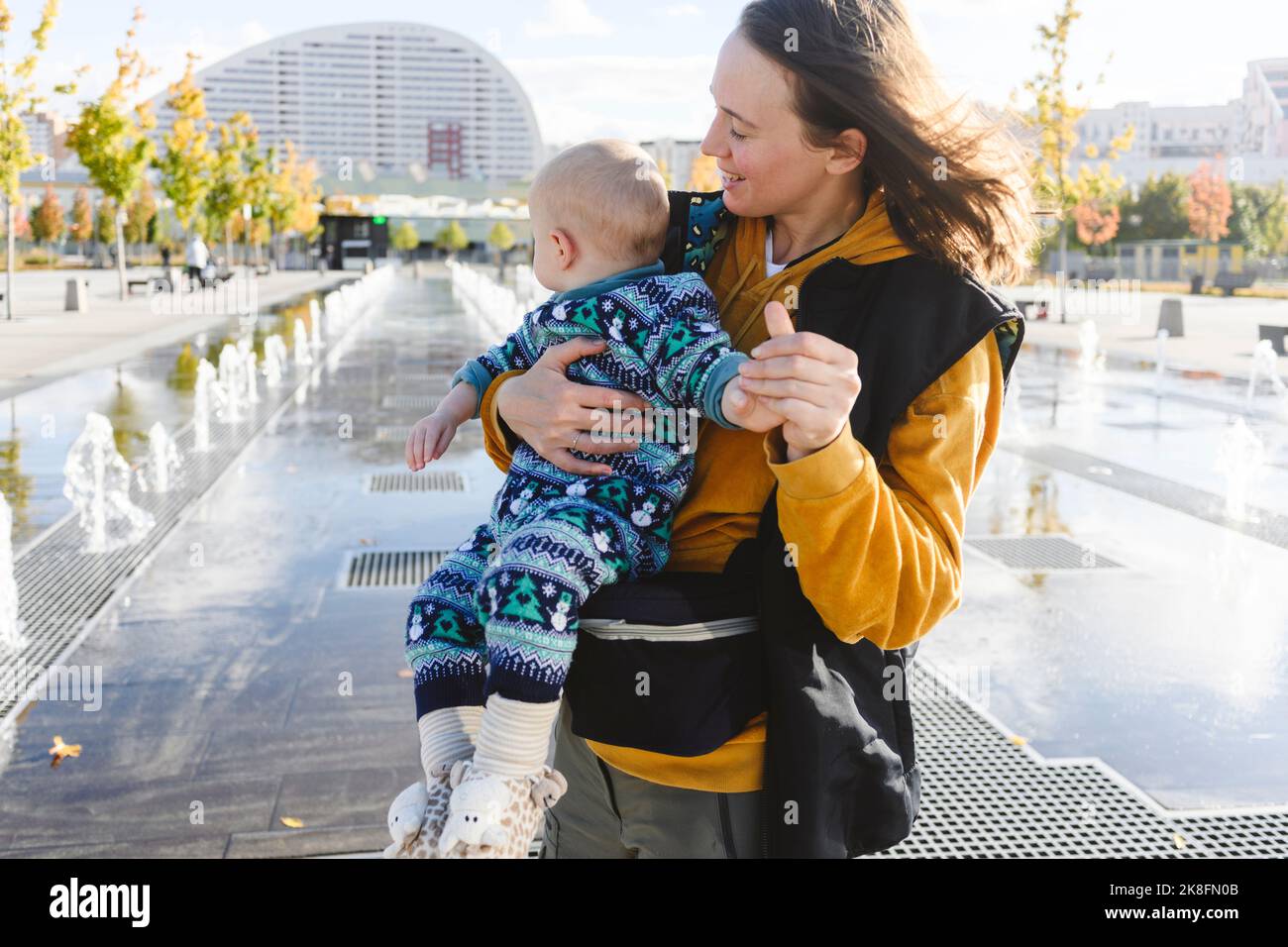 Madre che gioca con il figlio nel parco urbano vicino alle fontane Foto Stock