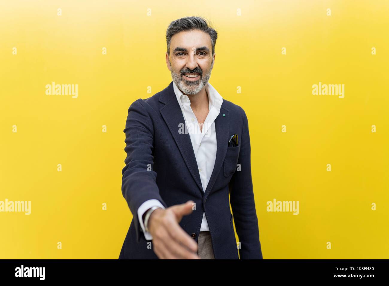 Uomo d'affari sorridente che fa la stretta di mano contro il muro giallo Foto Stock