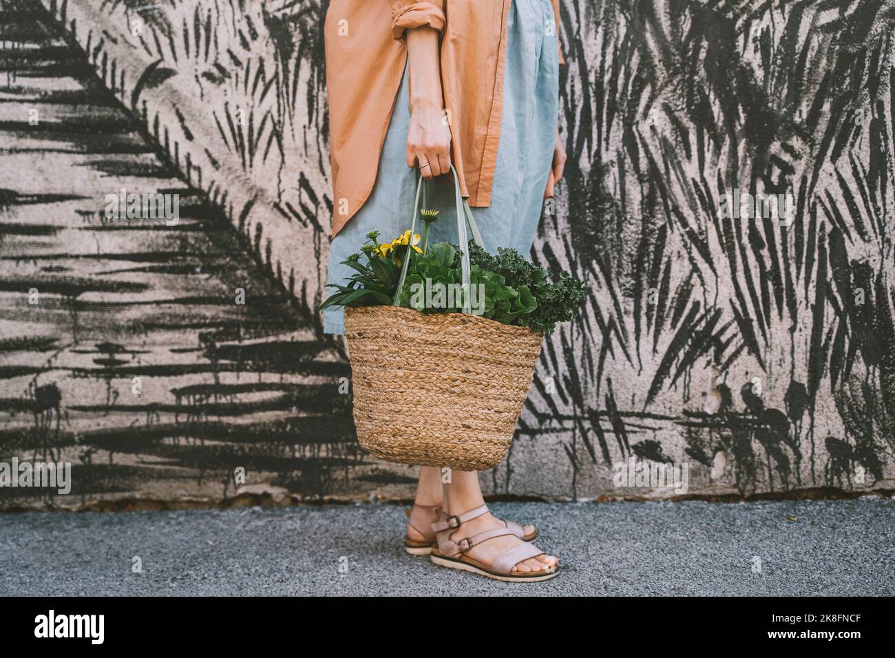 Donna con verdure a foglia e fiori in sacchetto di vimini da parete a motivi Foto Stock