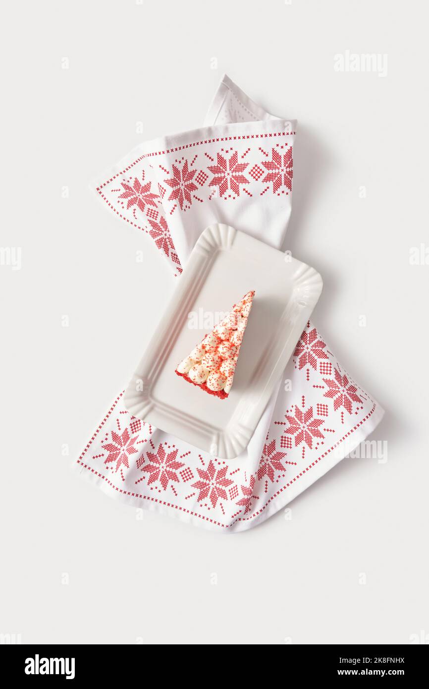 Fetta di torta di velluto rosso in vassoio bianco su tovagliolo da tavolo ricamato su sfondo bianco Foto Stock
