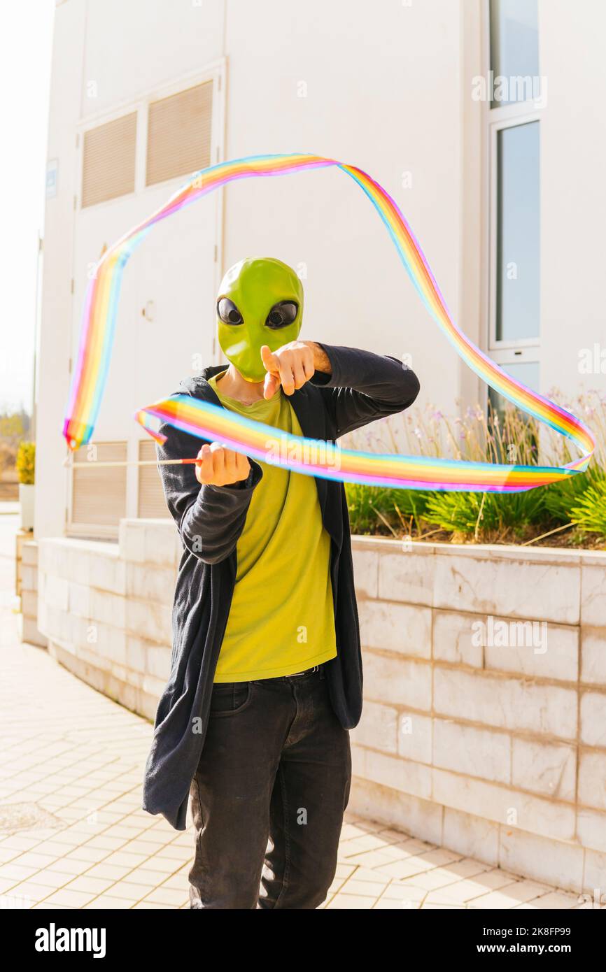 Uomo che indossa una maschera aliena giocando un nastro ritmico arcobaleno sul sentiero Foto Stock