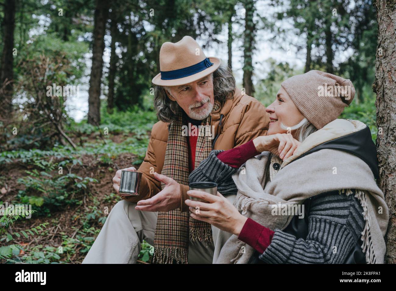 Donna con uomo anziano che ha il tè seduto nella foresta Foto Stock