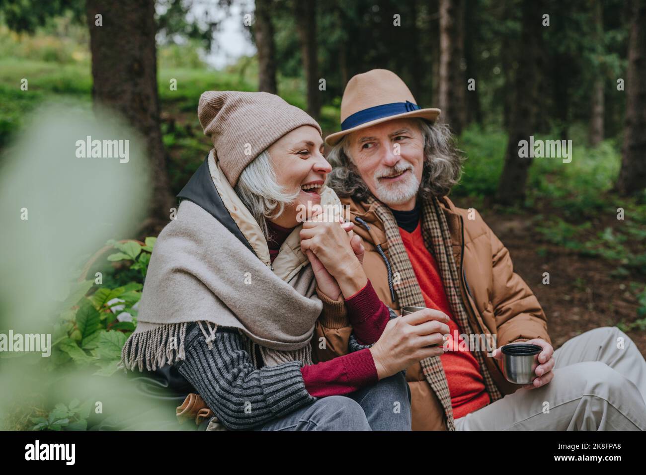 Donna matura sorridente con uomo anziano seduto nella foresta Foto Stock