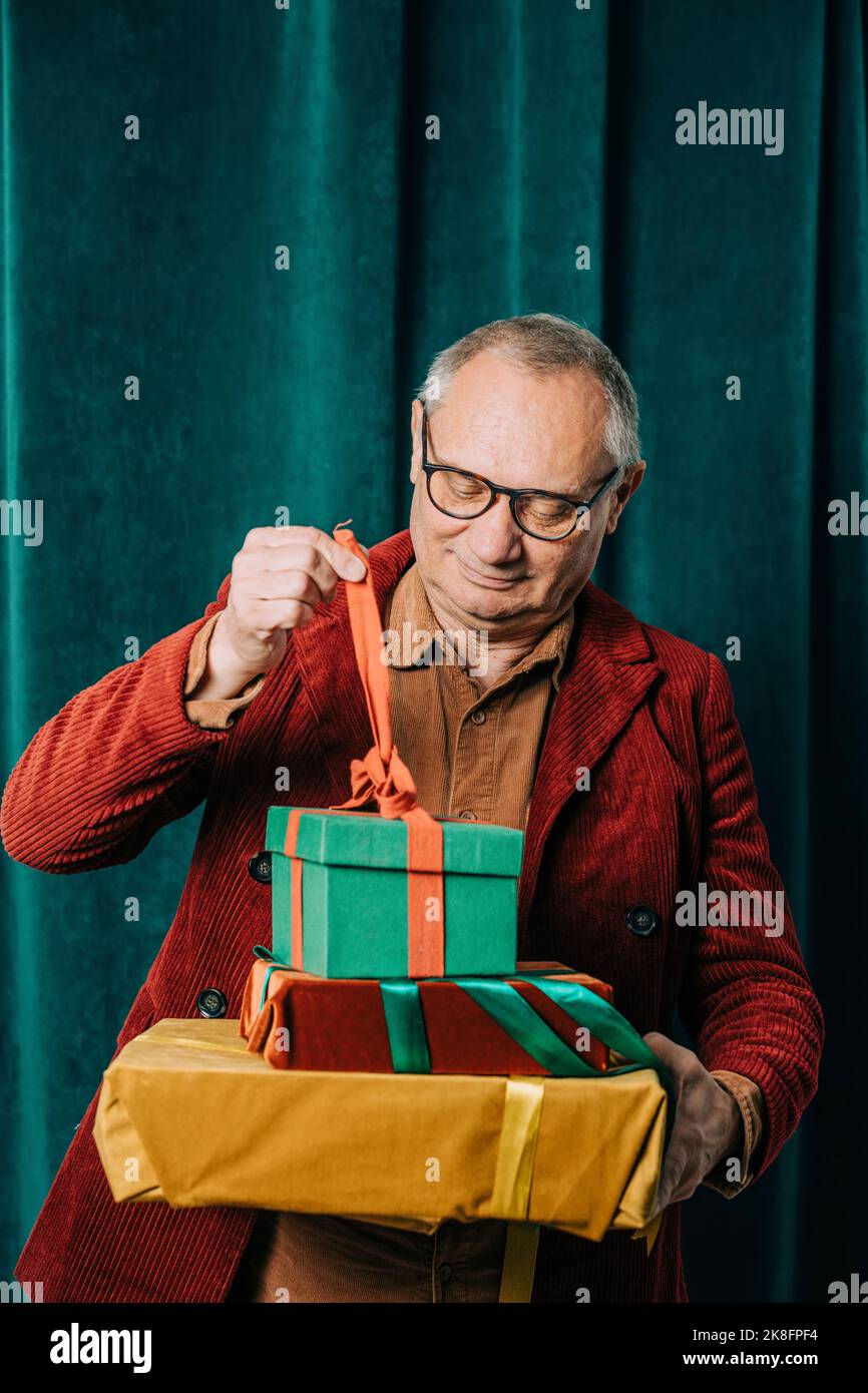 Felice uomo anziano apertura scatole regalo di fronte alla tenda Foto Stock