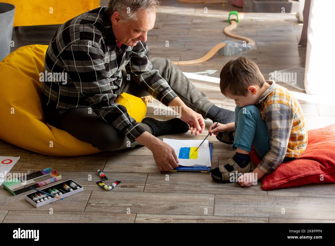 Buon nonno che insegna disegno della bandiera Ucraina al nipote a casa Foto Stock