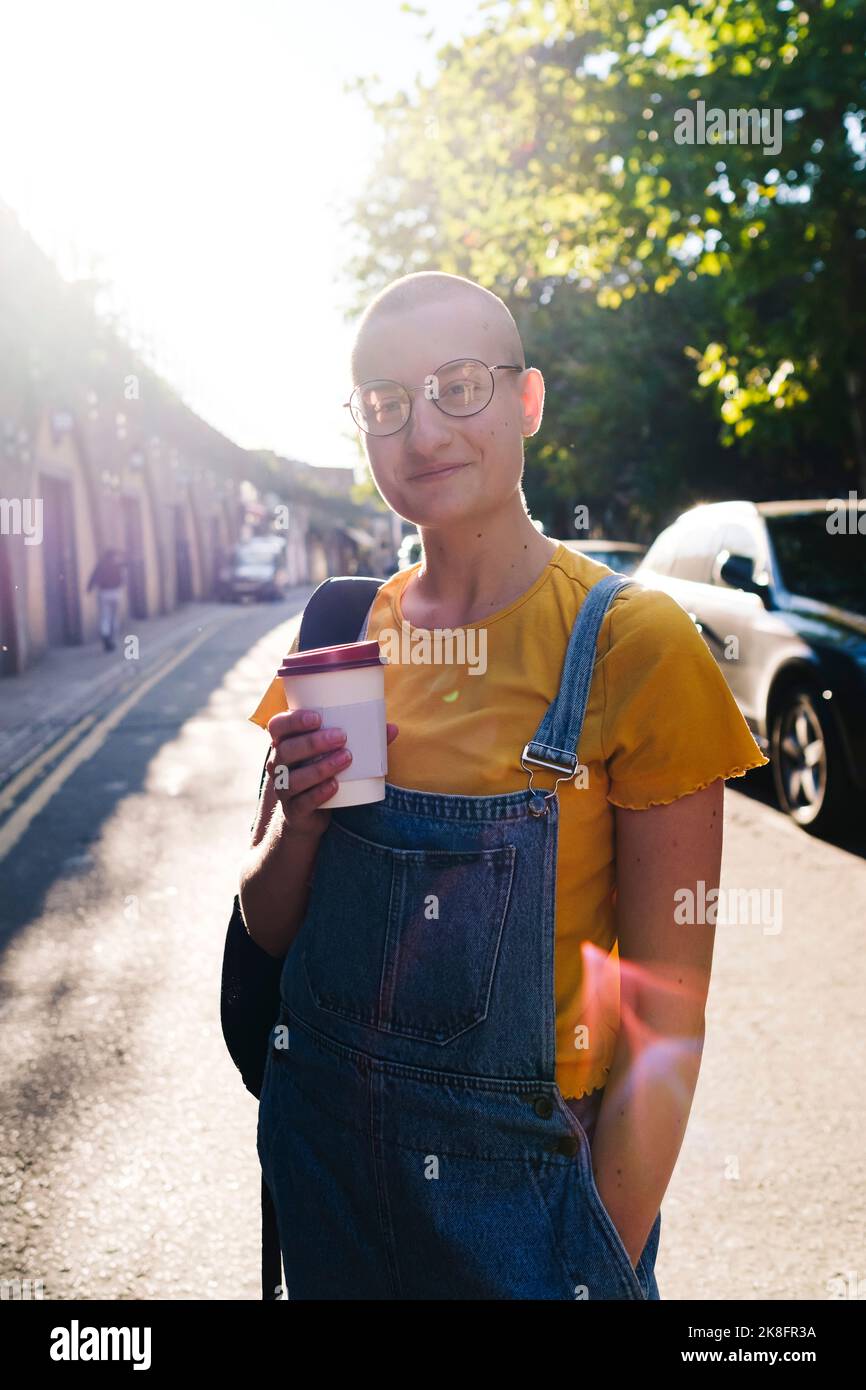 Persona sorridente androgina con una tazza di caffè usa e getta in piedi sulla strada Foto Stock