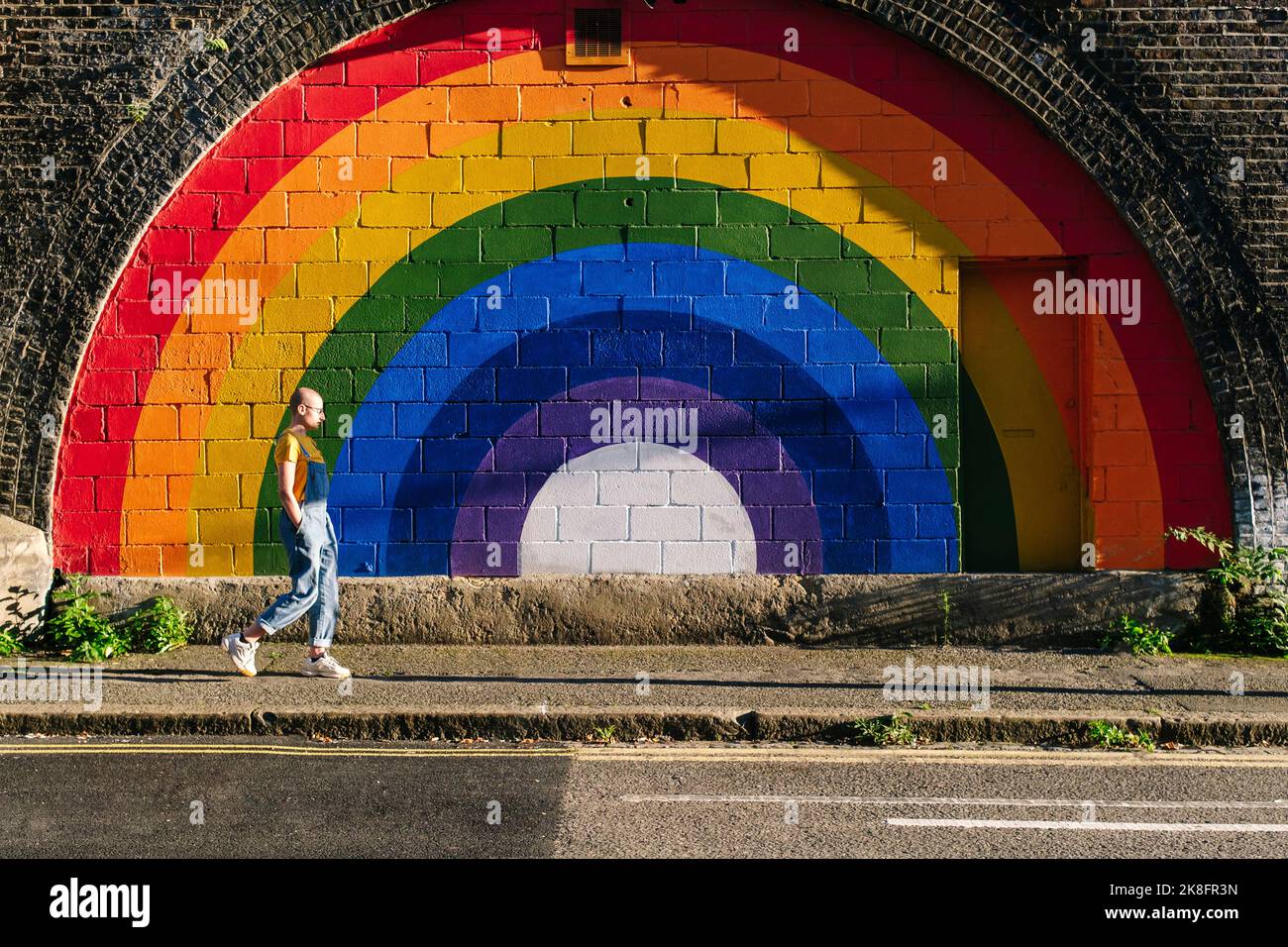 Giovane androgina che cammina sul sentiero vicino alla parete arcobaleno Foto Stock