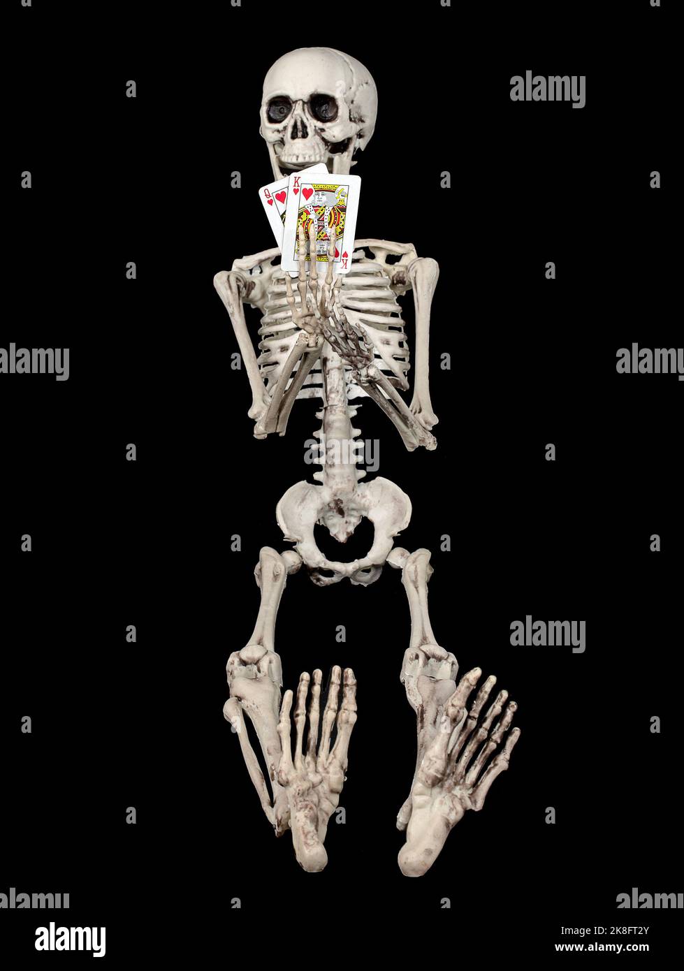 Scheletro che tiene un paio di carte da gioco su sfondo nero Foto Stock