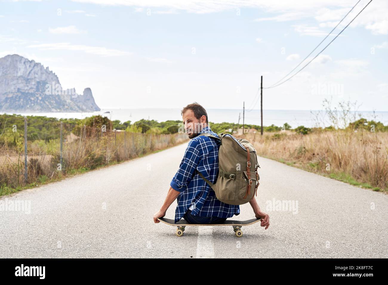 Uomo che indossa lo zaino seduto sullo skateboard Foto Stock