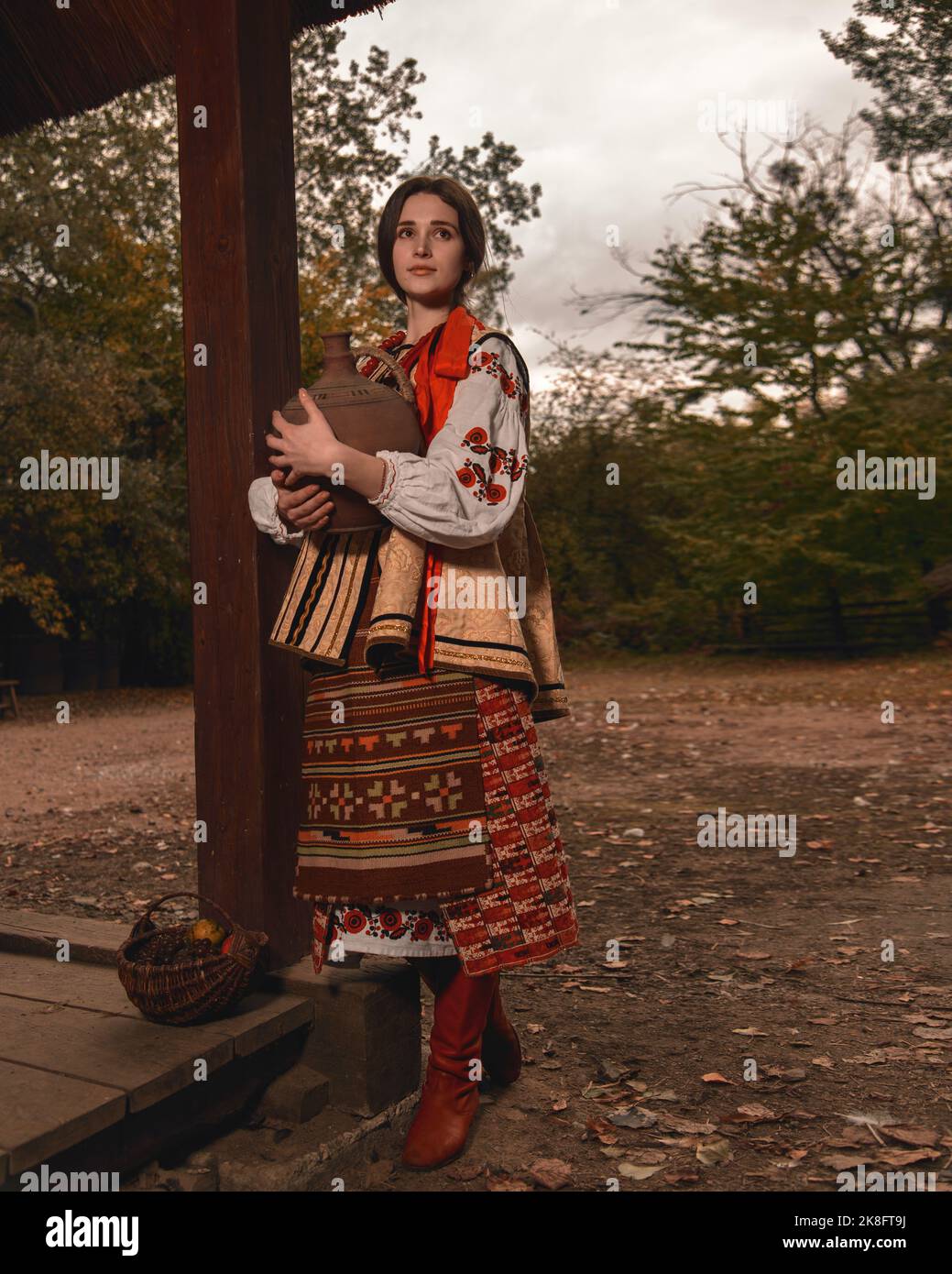 Pensivo bella giovane donna vestita tradizionale ucraino ricamato vestiti tenendo vecchio crock in mano guardando lontano. Vestito vintage Foto Stock