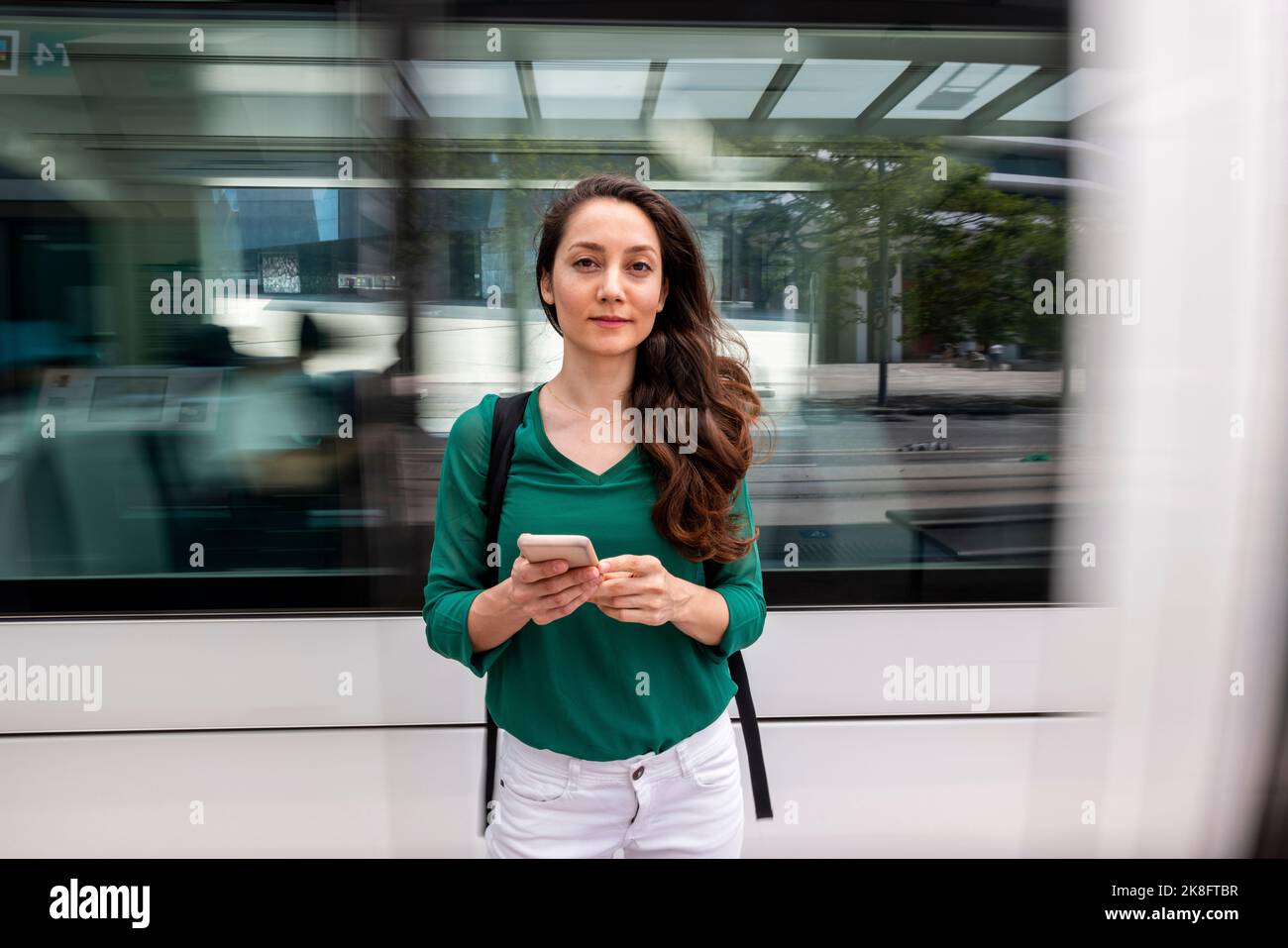 Donna sorridente in piedi con smartphone alla stazione del tram Foto Stock