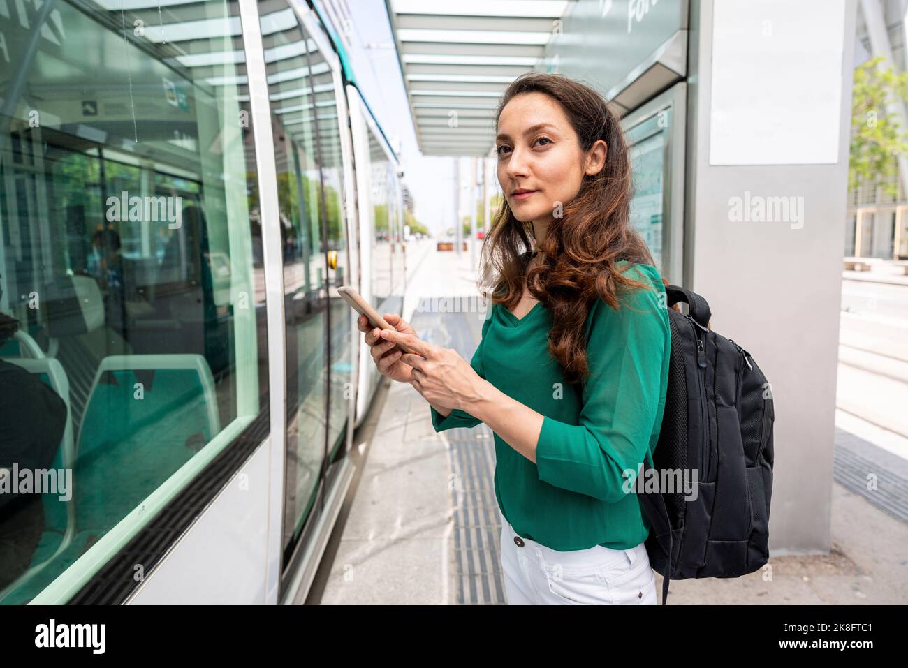 Donna sorridente con smartphone alla stazione del tram Foto Stock