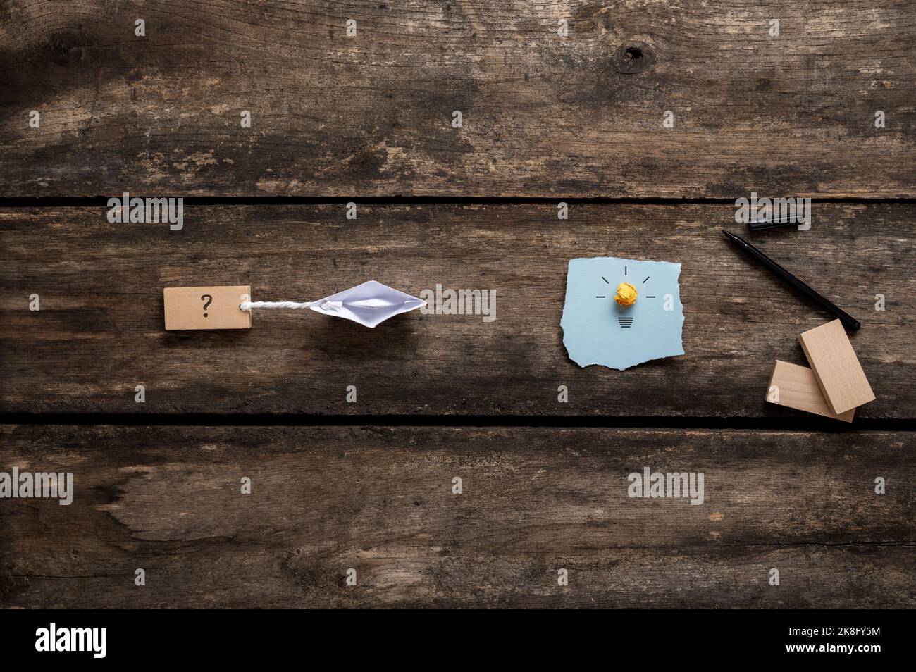 Immagine concettuale della visione e dell'idea di business e della strada verso l'obiettivo - origami fatto barca di carta tirando un segno punto interrogativo verso una lampadina. Foto Stock