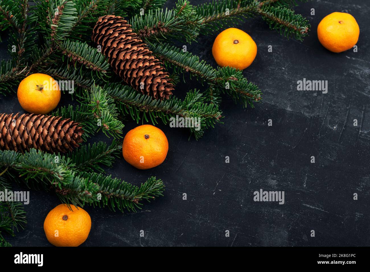 Sfondo natalizio con tangerini, rami di abete, coni su tavola nera. Vista dall'alto, spazio di copia Foto Stock