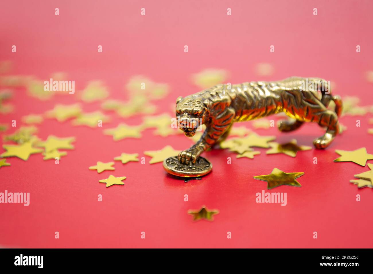 Una figura di bronzo di una tigre con una moneta su sfondo rosso e stelle dorate, copia spazio. Foto Stock