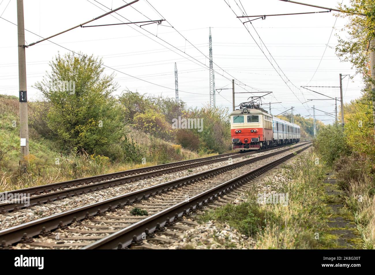 Un treno elettrico per passeggeri corre in una mattina d'autunno nebbiosa. Una linea ferroviaria nella Repubblica Ceca vicino al villaggio di Hradcany. Trasporto passeggeri in treno Foto Stock