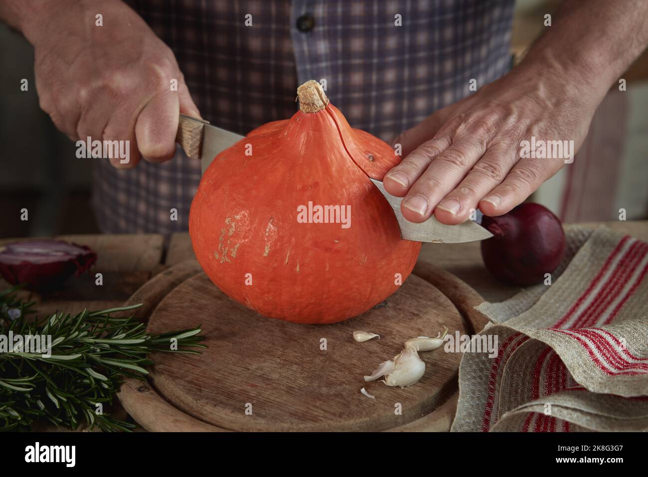 Raccolto anonimo maschio taglio zucca fresca con coltello affilato su tagliere di legno in cucina Foto Stock