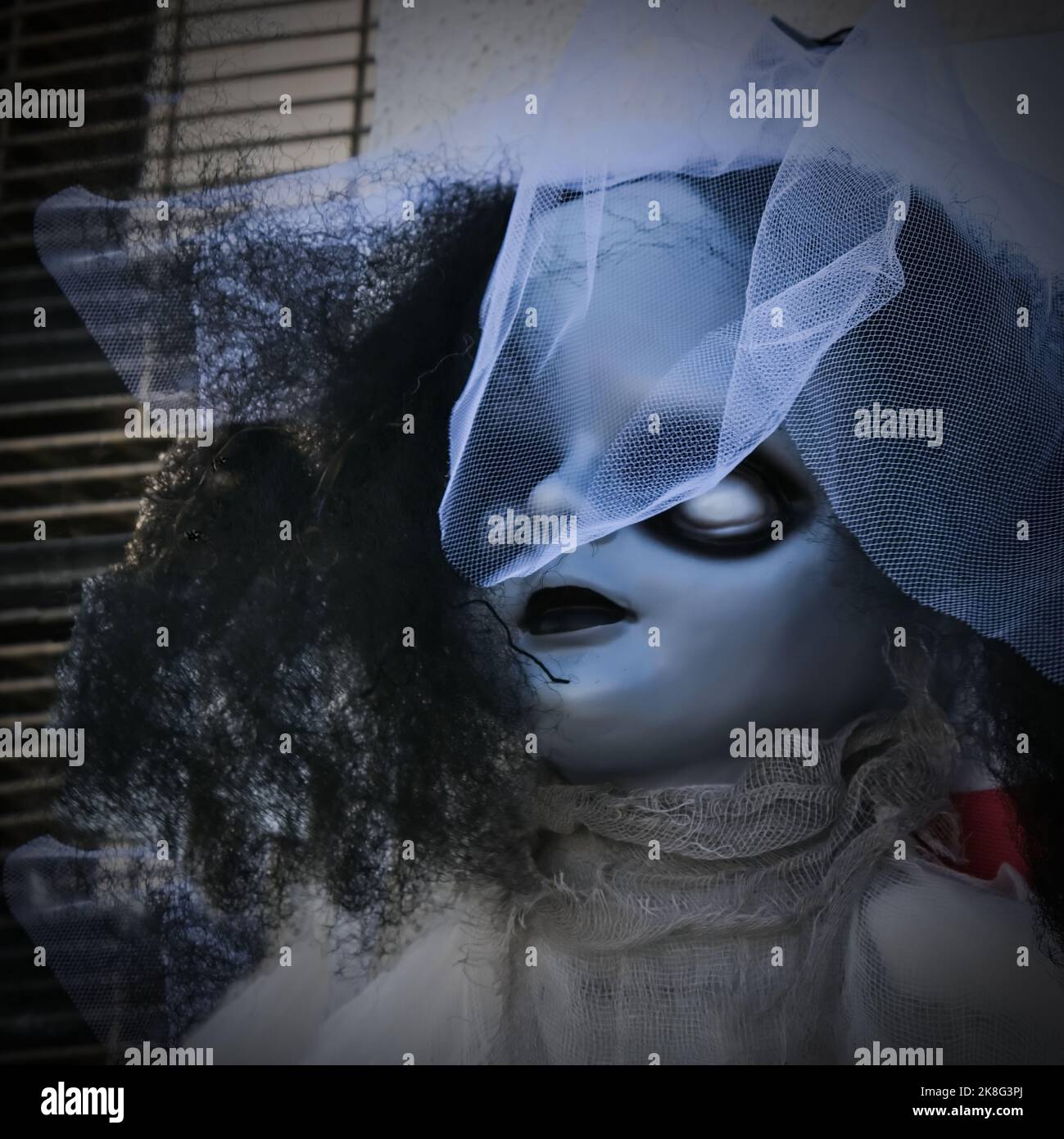 Bambola Horror vintage con occhielli bianchi che indossano un elegante cofano con velo. Faccia di bambola infestante del bambino. Sfondo di Halloween Foto Stock