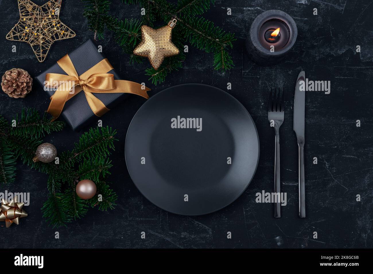 Tavolo elegante, scatola regalo, rami di abete, stella e palle con piatto nero, posate e candela su tavolo nero. Concetto di Natale. Vista dall'alto, piatta Foto Stock