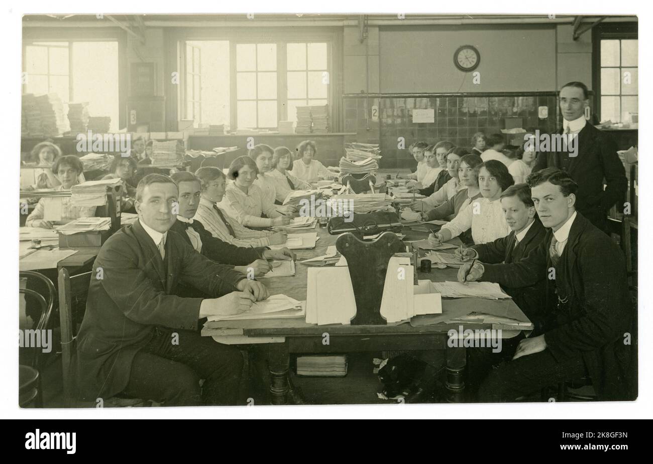 Originale primi del 1900, WW1 era cartolina di giovani impiegati, impiegati amministrativi, conti / amministrazione con personale sia maschile che femminile in un grande ufficio occupato e angusti, un sacco di documenti cartacei. Regno Unito circa 1913 Foto Stock