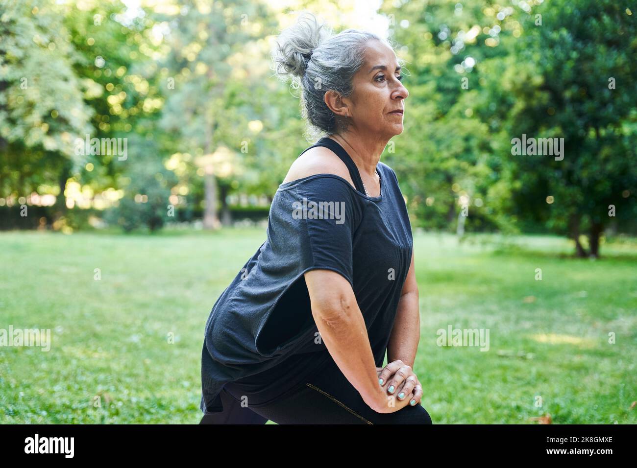 Atleta anziana femminile con gambe grigie che allungano i capelli nel parco Foto Stock