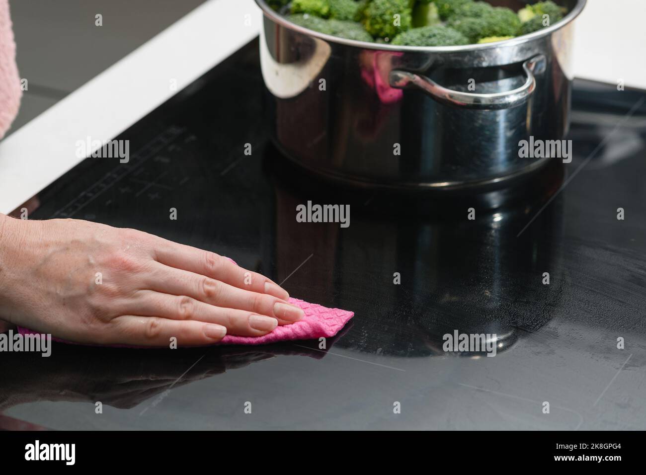 Donna pulizia a induzione top. La mano femminile pulisce il piano cottura del fornello a induzione. Foto Stock