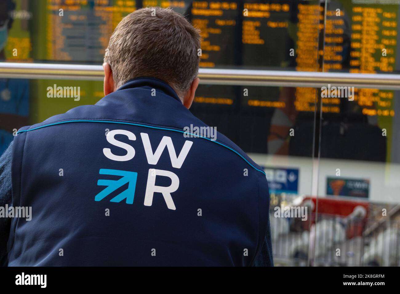 SWR, logo delle ferrovie del sud-ovest sulla giacca per dipendenti di fronte all'esposizione di Time boarding della stazione di waterloo, londra, regno unito Foto Stock