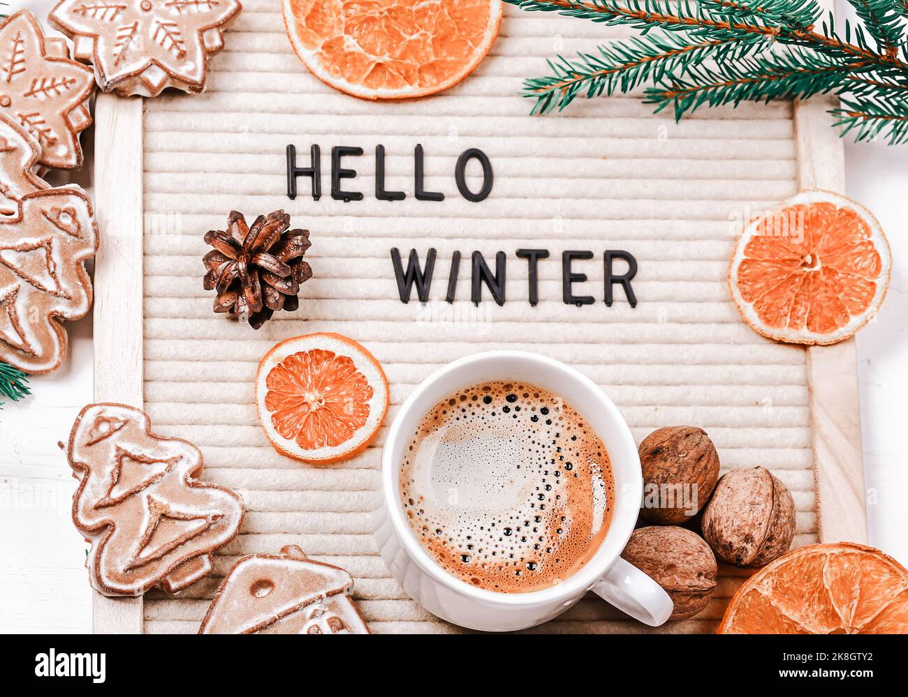 Scritta ciao inverno sulla tavola delle lettere. Rami di abete, arance secche, noci e una tazza di caffè. Sfondo minimalistico di nuovo anno 2023 Foto Stock