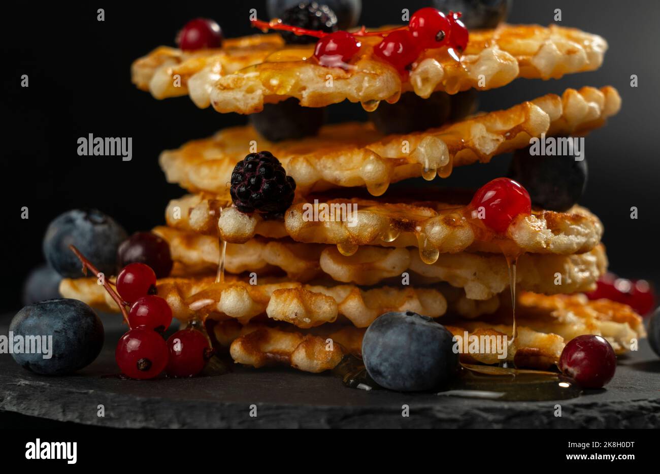 Gocce di miele fresco da freschi waffle belgi croccanti con mirtilli freschi, more e ribes rossi Foto Stock