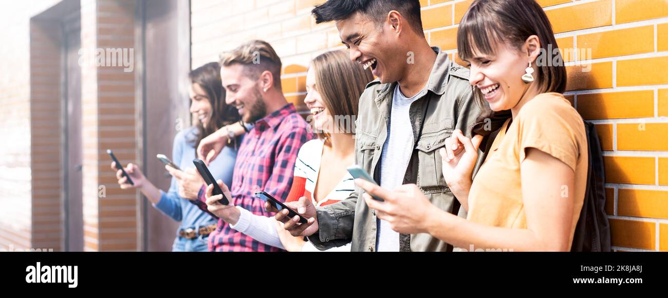 Banner orizzontale con amici multiculturali che ridono utilizzando lo smartphone alle pareti del campus universitario - concetto di tecnologia con sempre connesso Foto Stock