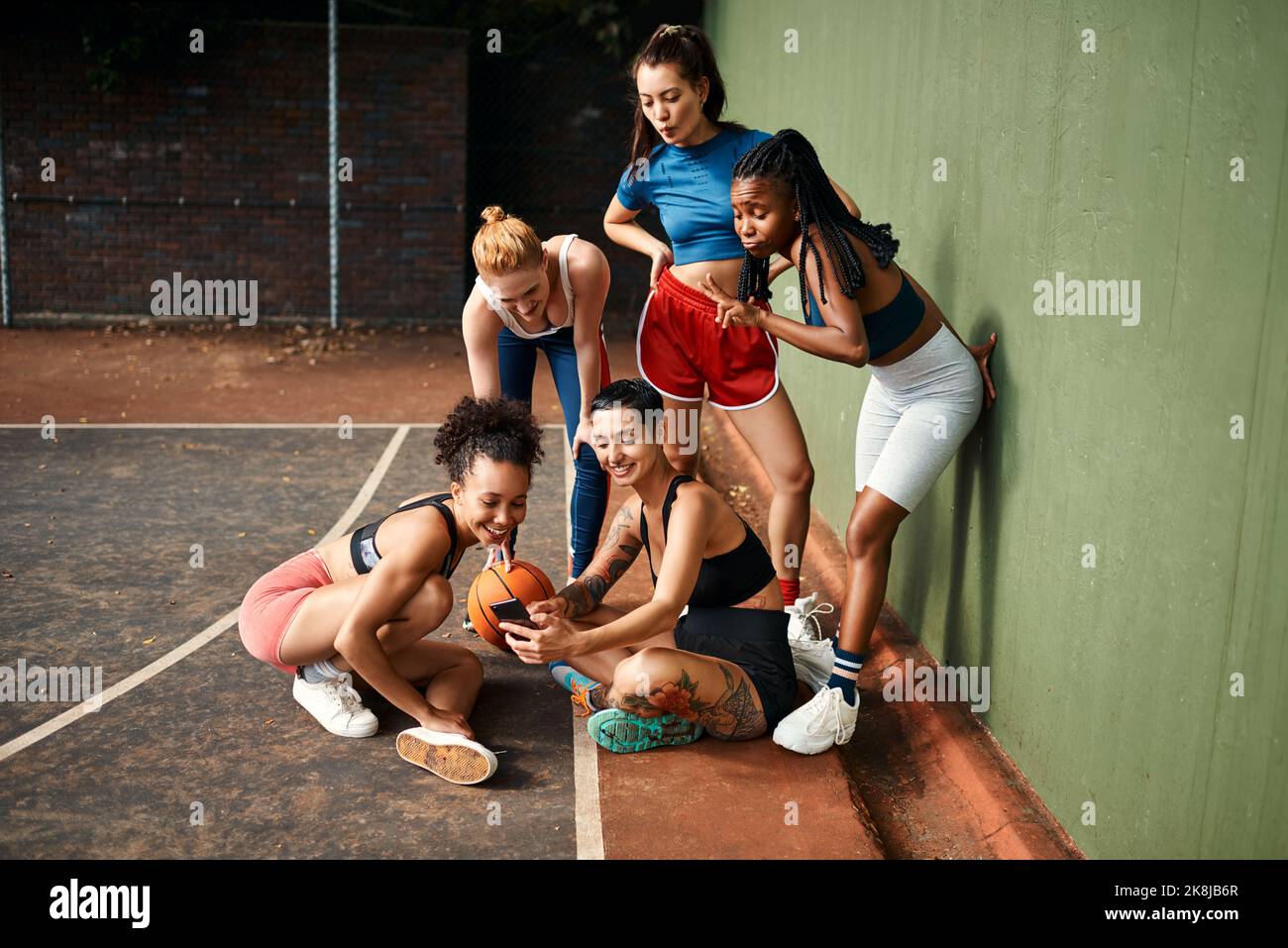 Un ultimo selfie di squadra. Un gruppo di sportivi diversi seduti insieme per un selfie dopo una partita di basket durante il giorno. Foto Stock