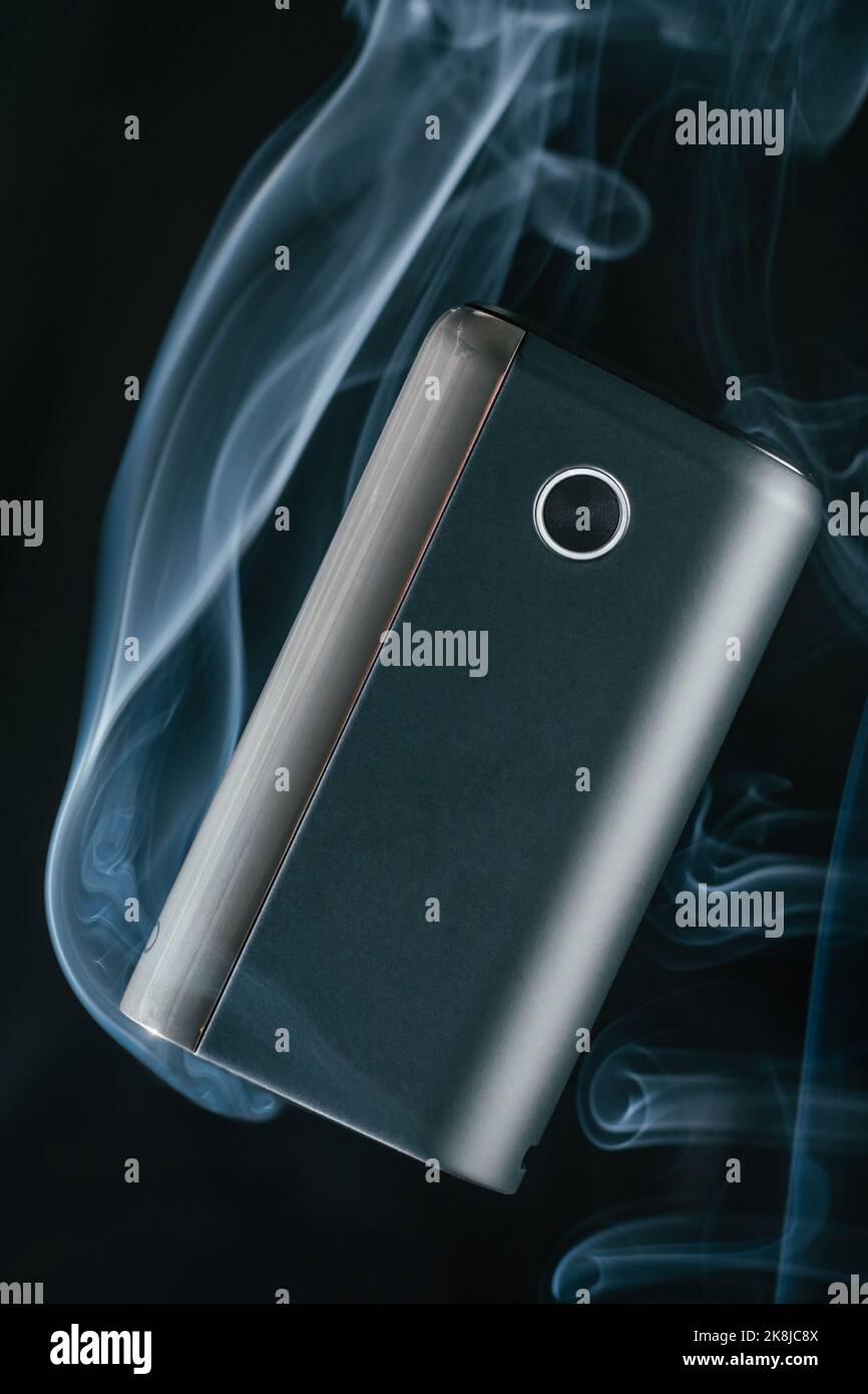 Il nuovo dispositivo di riscaldamento per fumo nero GLO galleggia in soffi di fumo bianco al neon blu. Sigarette elettroniche moderne Foto Stock