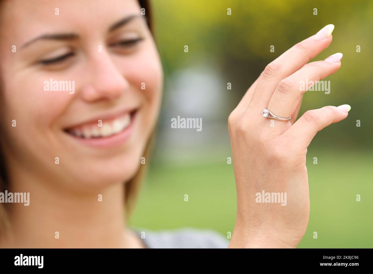 Felice giovane fidanzata che guarda il suo anello di fidanzamento in un parco Foto Stock
