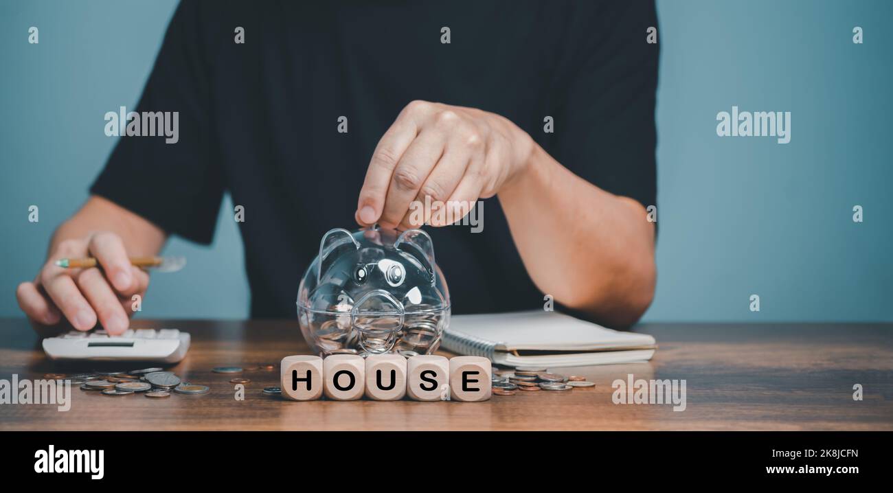 Accumulazione di soldi per l'alloggiamento, ipoteche, alloggiamento acquistabile, il sogno di possedere una casa, le rate di prestito, mano ha messo una moneta nella banca del piggy Foto Stock