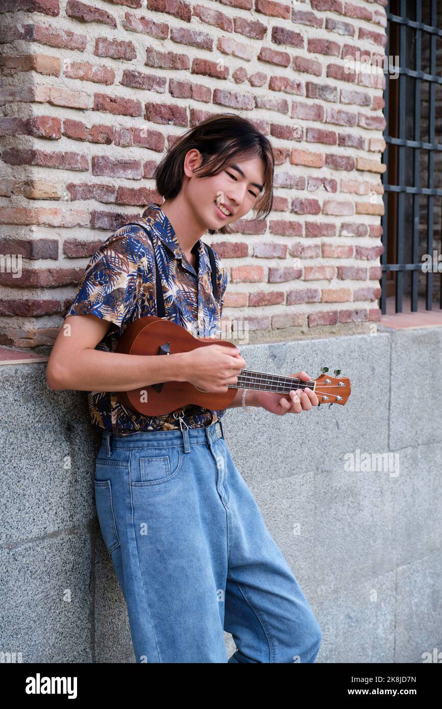 Ragazzo asiatico sorridente e suona la chitarra acustica Ukulele. Foto Stock