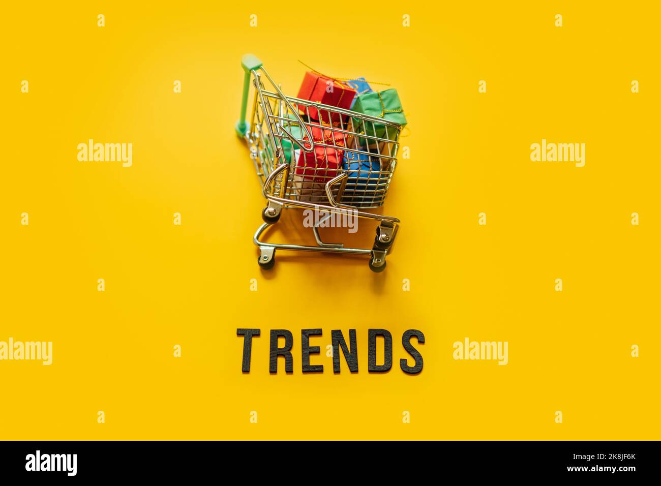 Concetto di tendenze dell'eCommerce Retail Shopping. Word Trends e mini carrello con scatola su sfondo giallo. Foto Stock