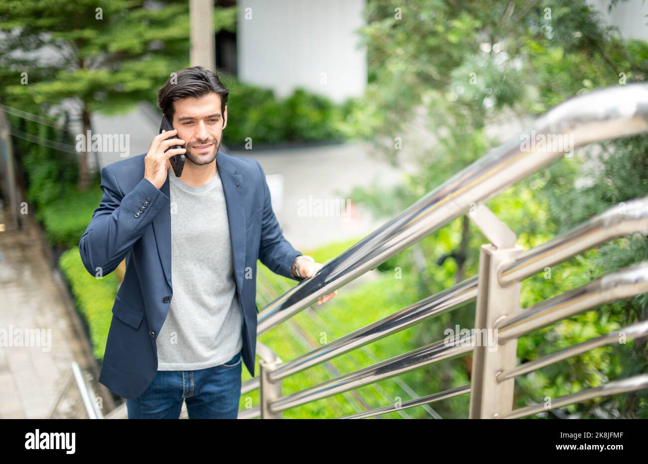 L'uomo d'affari che parla con lo smartphone mentre è in viaggio. Sentendosi felice e rilassante, un giovane uomo d'affari casual che indossa una giacca da tuta. Foto Stock